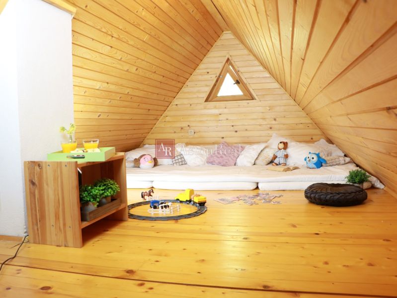 Der Dachboden der Hütte mit einem Boden in Holzoptik enthält Matratzen, Spielzeug und einen Tisch.