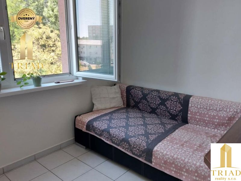 Ein Sofa in der Ecke des Zimmers mit offenem Fenster und Blumen auf der Fensterbank.