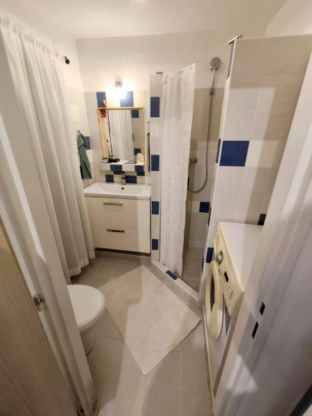 Badezimmer in einer Einzimmerwohnung mit Waschmaschine, Duschkabine und Waschbecken.