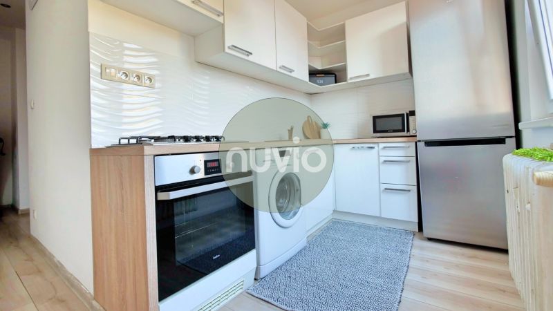 Küche in einer 2-Zimmer-Wohnung mit weißen Schränken und einem Boden in Holzoptik.