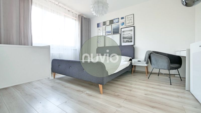 Helles Schlafzimmer mit Bett, Sessel und Boden in Holzoptik, in einer 2-Zimmer-Wohnung.