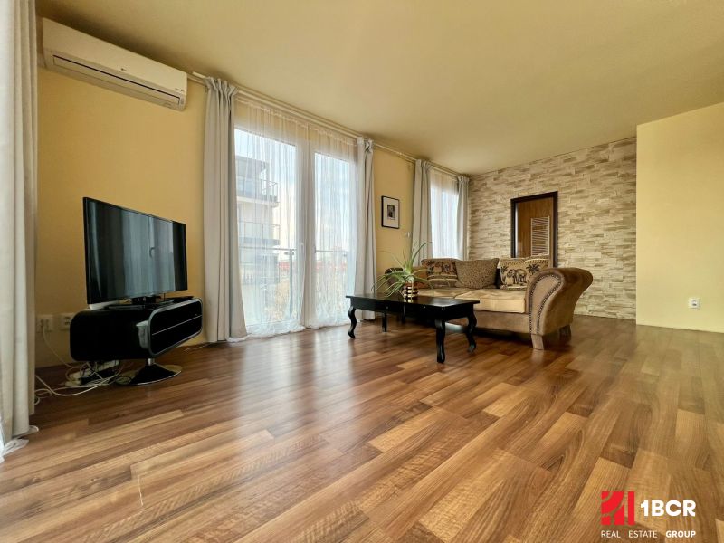 Wohnzimmer in einer 2-Zimmer-Wohnung mit Holzboden, Fernseher und bequemer Couch.
