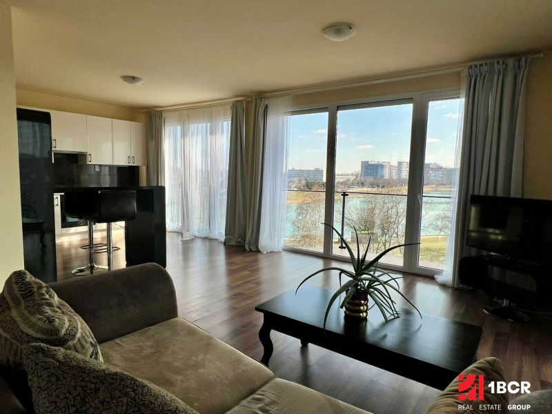 Wohnzimmer in einer 2-Zimmer-Wohnung mit großen Fenstern und einem Boden in Holzoptik.