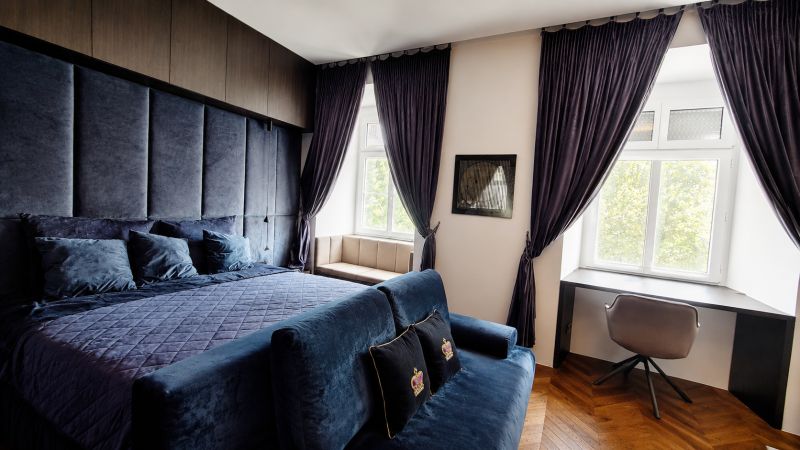 Luxuriöses Schlafzimmer mit dunklen Vorhängen und Schreibtisch in einer 2-Zimmer-Wohnung.