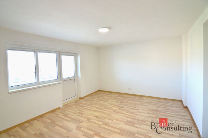 Ein helles Zimmer in einer 2-Zimmer-Wohnung mit Holzboden und großen Fenstern.
