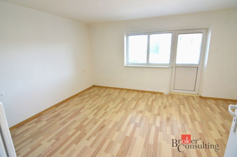 Helles Zimmer mit Holzboden in einer 2-Zimmer-Wohnung mit Zugang zum Balkon.