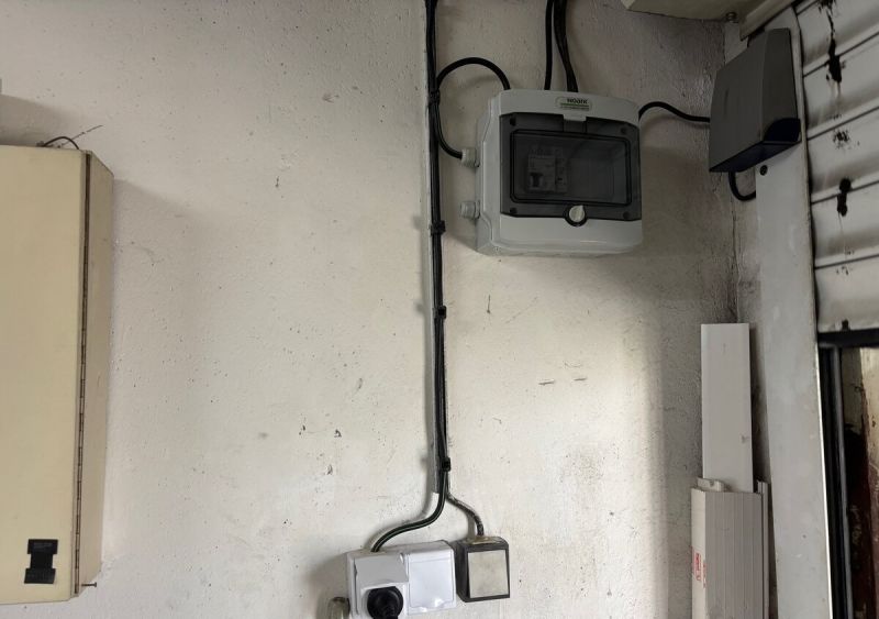 Elektroinstallation in der Garage mit einem Schrank und Kabeln an der Wand.