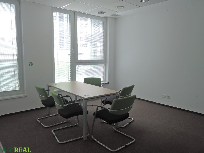 Büros mit Teppichboden, Konferenztisch, grüne Stühle, natürliches Licht.