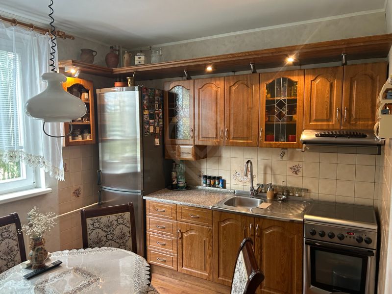 Küche in einer 3-Zimmer-Wohnung mit Holzmöbeln, dekorativem Vorhang und Esstisch.