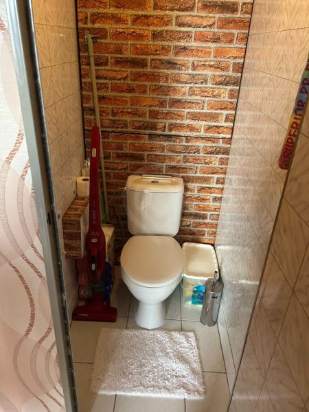 Badezimmer in einer 3-Zimmer-Wohnung mit Toilette, Ziegelmuster und Reinigungsmitteln.