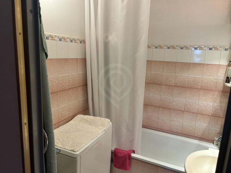 Badezimmer mit Badewanne, Waschmaschine mit Handtuch und Fliesen in einer 3-Zimmer-Wohnung.