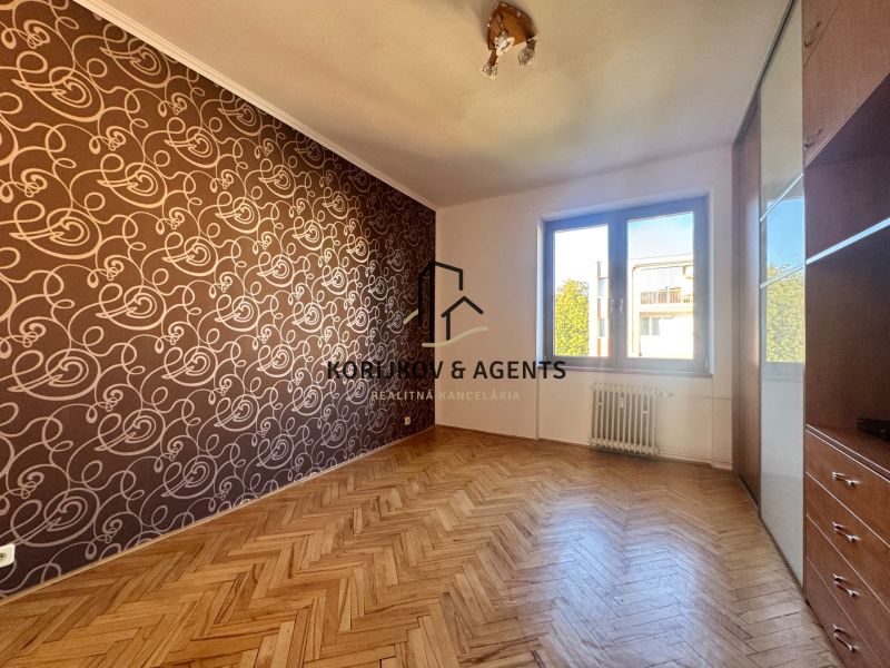 Ein Zimmer in einer 4-Zimmer-Wohnung mit einem Boden in Holzoptik und gemusterten Tapeten.