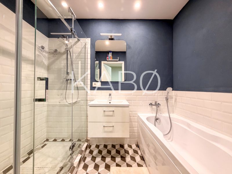 Badezimmer in einer 2-Zimmer-Wohnung mit Duschkabine, Badewanne und weißen Fliesen.