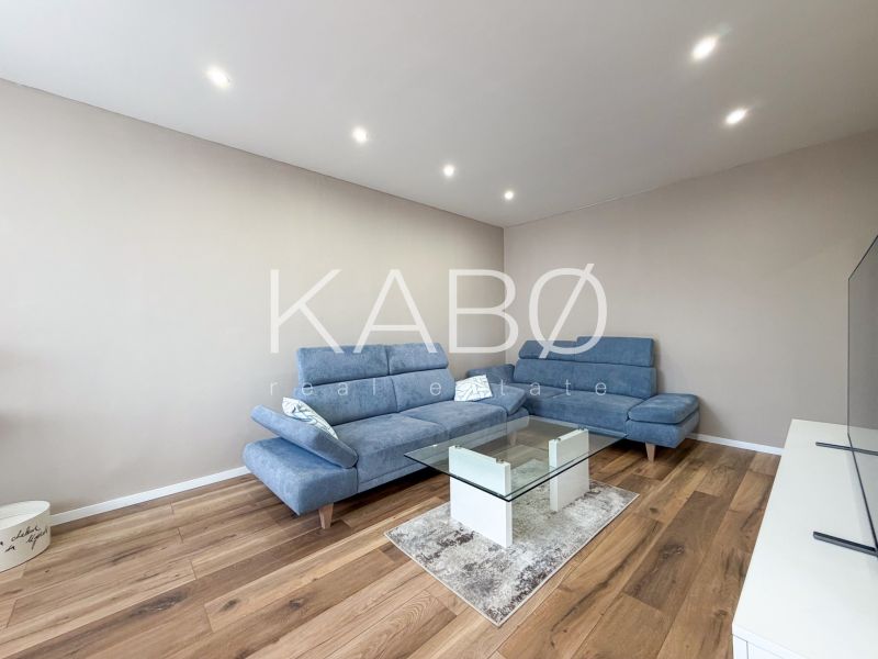 Wohnzimmer mit blauer Couch und Glastisch, Boden mit Holzdekor.