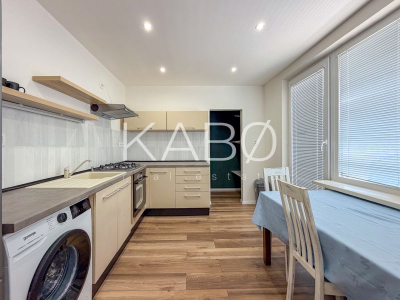 Küche in einer 2-Zimmer-Wohnung mit Geräten, Esstisch und Bodenbelag in Holzoptik.