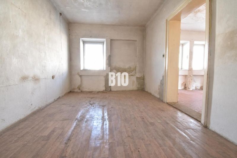 Ein Raum in einem Einfamilienhaus mit einem Boden in Holzoptik und einer beschädigten Wand.