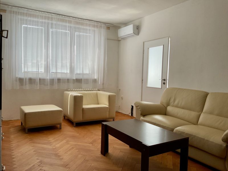 Wohnzimmer in einer Zweizimmerwohnung mit cremefarbenem Sofa und Boden in Holzoptik.