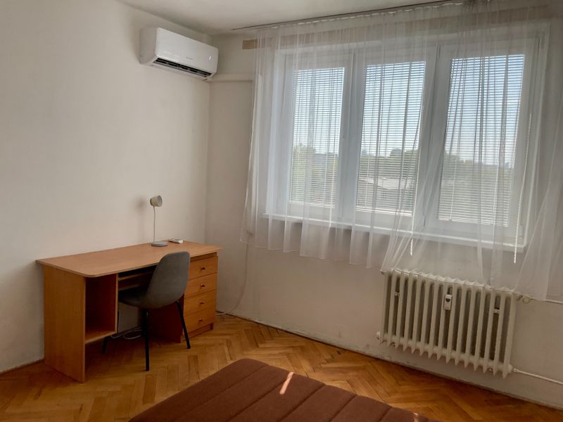 Ein Zimmer in einer 2-Zimmer-Wohnung mit einem Schreibtisch, einem Stuhl und einer Klimaanlage.