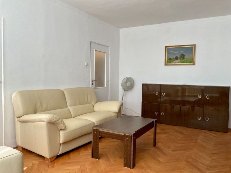 Wohnzimmer mit cremefarbenem Sofa, Holztisch und Schrank auf einem Boden mit Holzdekor.