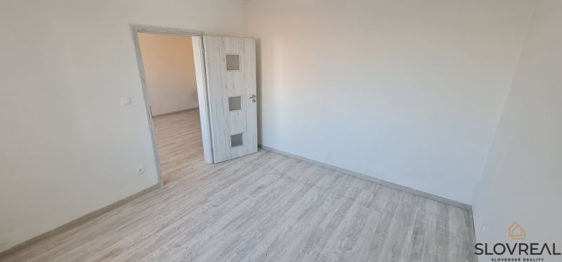Ein Zimmer mit einem Boden in Holzoptik und weißen Türen in einer Zweizimmerwohnung.