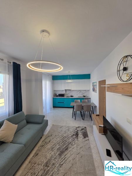 Wohnzimmer einer 2-Zimmer-Wohnung mit stilvoller Beleuchtung, Küche und bequemer Couch.