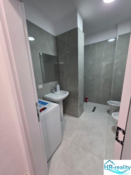 Badezimmer in einer 2-Zimmer-Wohnung mit Duschkabine, Waschmaschine und Keramikfliesen.