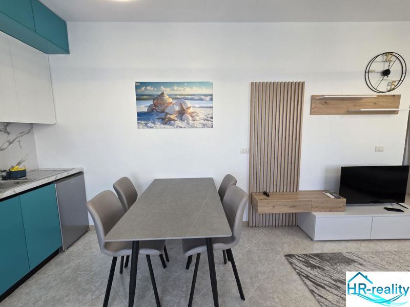 Helle Küche in einer 2-Zimmer-Wohnung mit Tisch, Muschelbild und Fernseher.