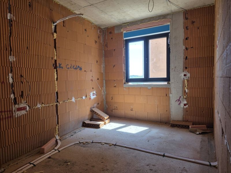 Unvollendetes Zimmer in einer 3-Zimmer-Wohnung mit freiliegenden Ziegelwänden und einem Fenster.