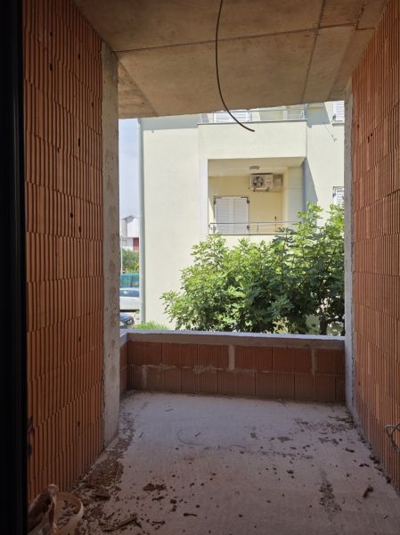 Ein unvollendeter Balkon in einer 3-Zimmer-Wohnung mit Blick auf Grünflächen und ein Nachbargebäude.