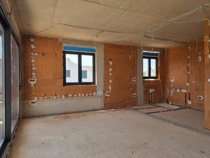 Innenraum einer im Bau befindlichen 3-Zimmer-Wohnung mit nackten Ziegelwänden und Kunststofffenstern.
