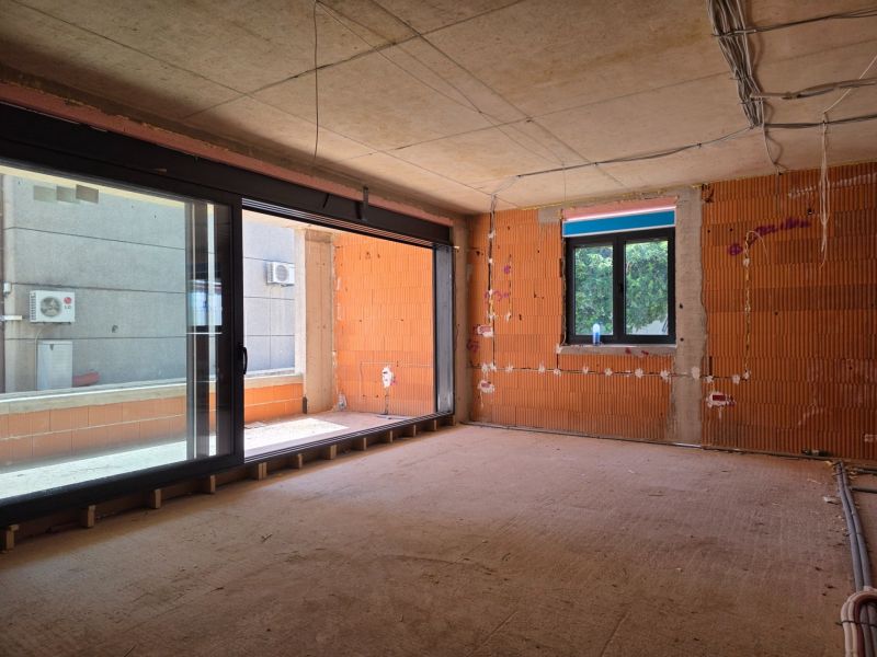 Unvollendete 3-Zimmer-Wohnung mit großen Fenstern und freiliegenden Ziegeln ohne Boden.