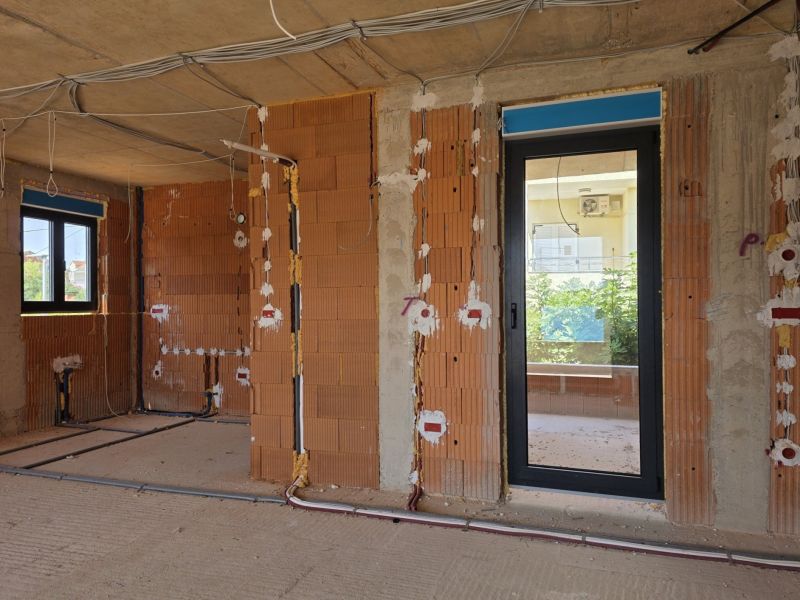 Unvollendete 3-Zimmer-Wohnung mit Ziegelwänden und Elektroinstallation, die zur Montage vorbereitet ist.