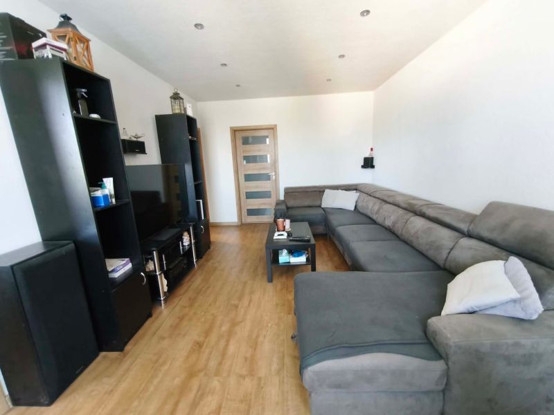 Wohnzimmer mit großer Couch, Holzboden und schwarzen Möbeln in einer 3-Zimmer-Wohnung.