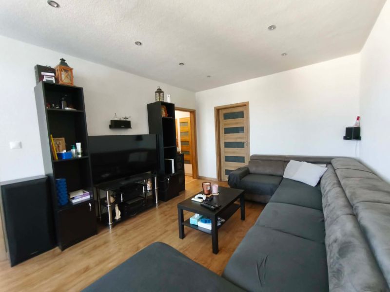 Wohnzimmer in einer 3-Zimmer-Wohnung mit großem Sofa, Fernseher und Holzboden.