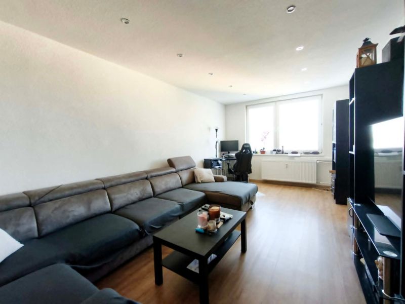Wohnzimmer in einer 3-Zimmer-Wohnung mit Holzboden, Sofa und PC-Tisch.