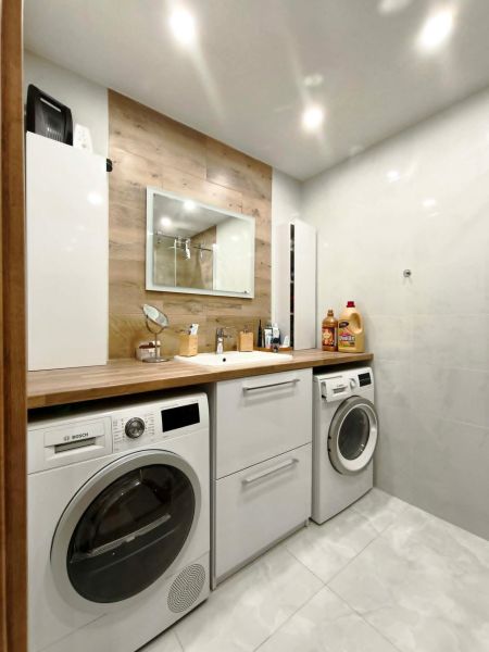 Badezimmer in einer 3-Zimmer-Wohnung mit Waschmaschine, Trockner und Boden mit Holzdekor.