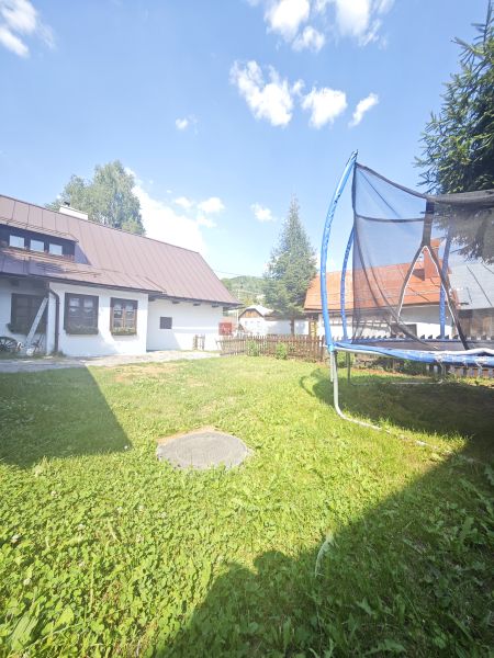 Eine Hütte in Špania Dolina mit einem Trampolin im grasbewachsenen Garten unter blauem Himmel.