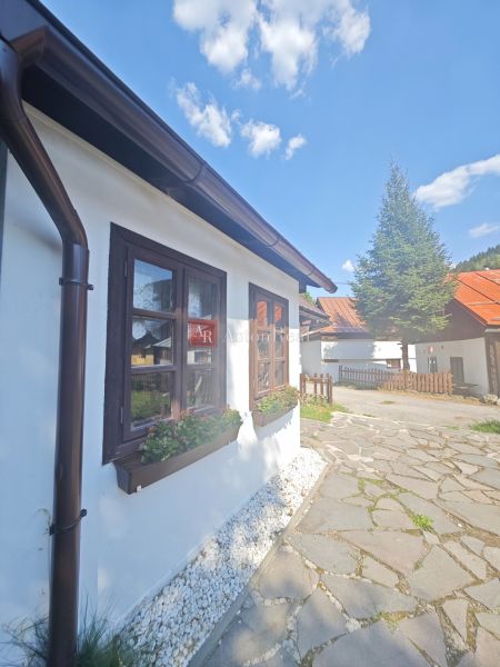 Eine Hütte in Špania Dolina mit einem Blumenbeet am Fenster und einem gepflasterten Weg.