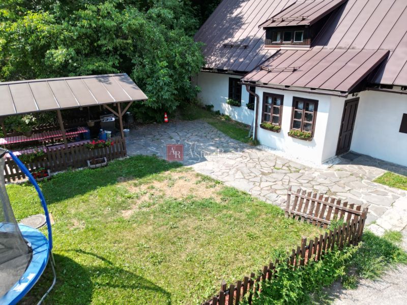 Ein Einfamilienhaus in Špania Dolina mit Garten, Rasen, Trampolin und einem hölzernen Pavillon in der Natur.