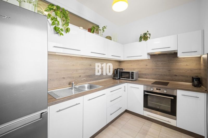 Küche in einer 2-Zimmer-Wohnung mit weißen Schränken und Holzelementen.