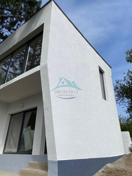 Ein Ferienhaus in Šahy mit markanten Verglasungen und weißer Fassade.