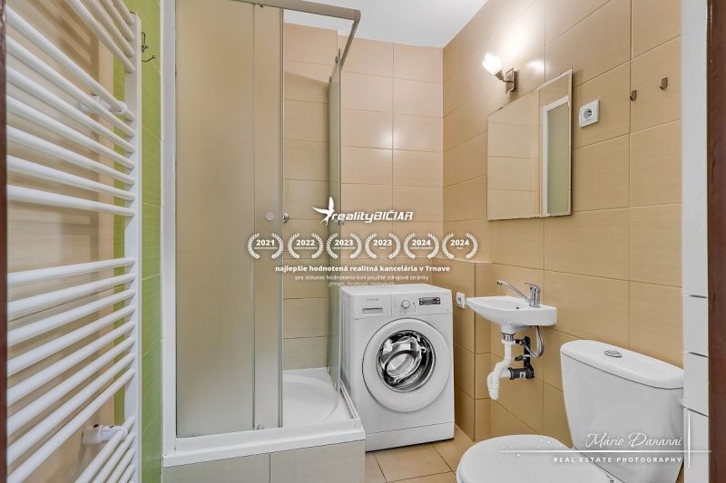 Badezimmer in einer Einzimmerwohnung mit Duschkabine und Waschmaschine, beige Fliesen.