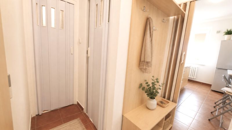 Flur in einer 2-Zimmer-Wohnung mit eingebautem Holzstauraum und Vorhängen.