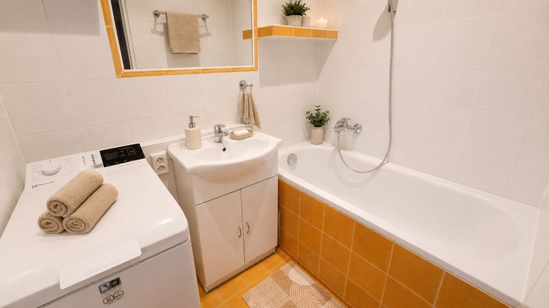 Badezimmer mit Badewanne, Waschbecken, Waschmaschine und dekorativen Handtüchern in einer 2-Zimmer-Wohnung.