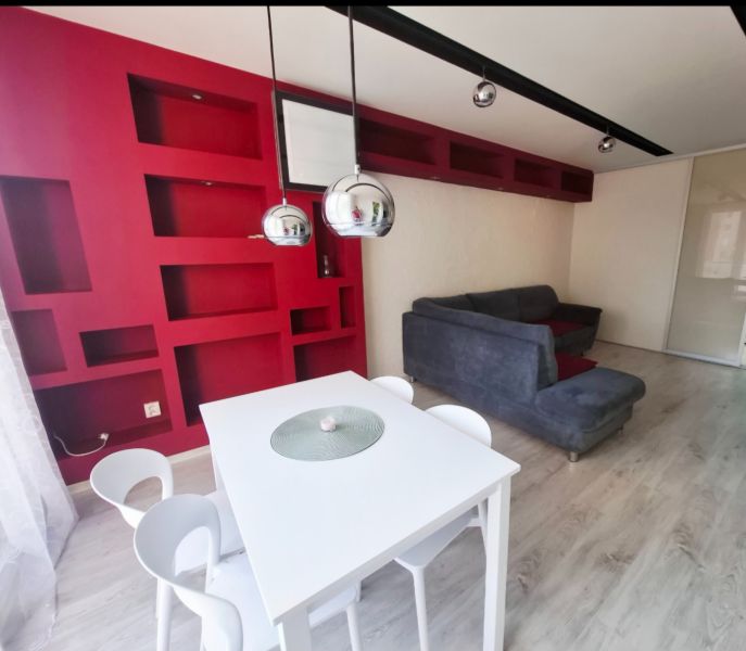 Innenraum einer 3-Zimmer-Wohnung mit roten Regalen, einem weißen Tisch und einem grauen Sofa.