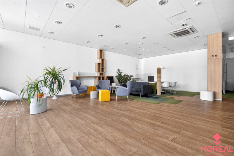 Geschäftsräume mit Sesseln, Pflanzen und einem Boden in Holzoptik, die komfortable Sitzgelegenheiten bieten.