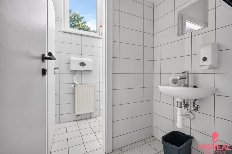 Toilette mit weißen Fliesen und Waschbecken in Geschäftsräumen.