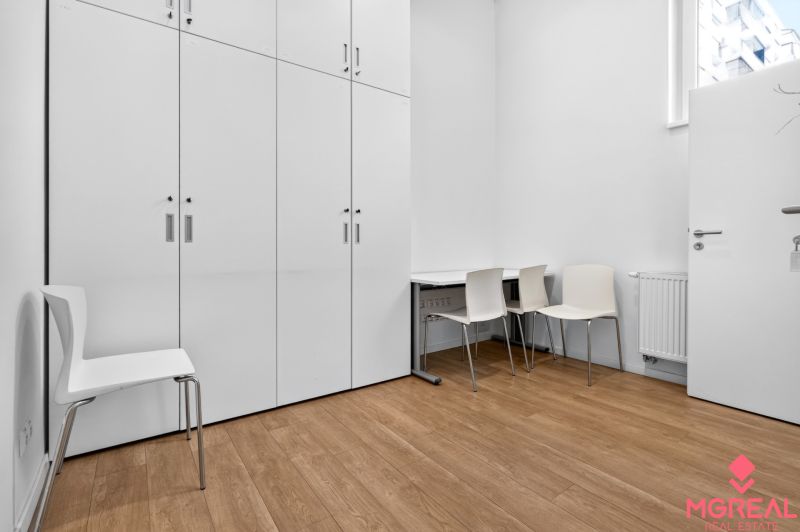 Weiße Schränke, Stühle und Tisch auf einem Boden mit Holzdekor in Geschäftsräumen.