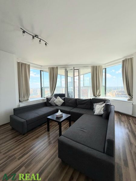 Geräumiger Wohnbereich mit dunklem Sofa und Boden in Holzoptik in einer 3-Zimmer-Wohnung.