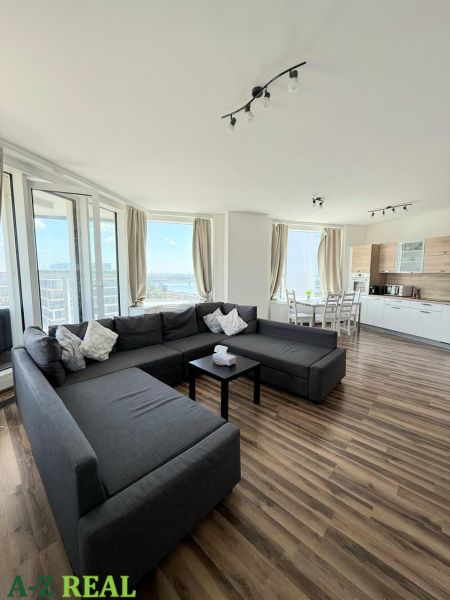 Wohnzimmer mit großer Couch, Esstisch und Boden mit Holzdekor.